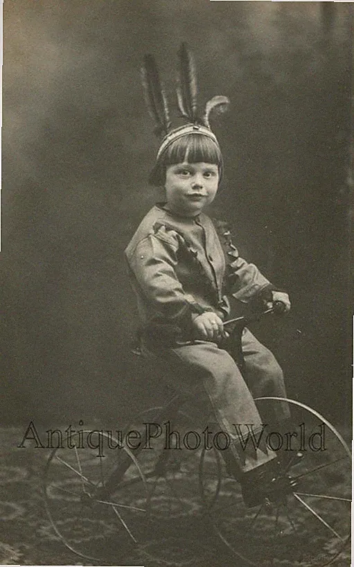 Cute boy as Indian w feather headdress on iron tricycle bicycle antique photo